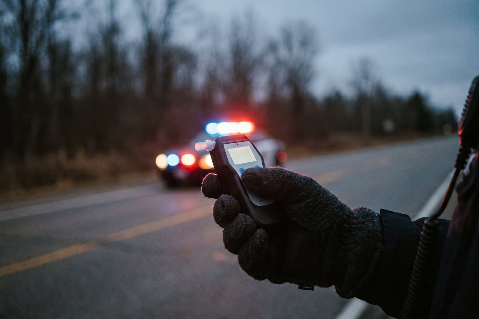 Police officer gloved hand holding a roadside screening device at a traffic stop at dusk